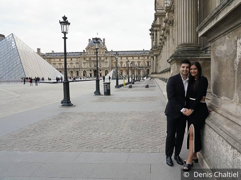 Un jeune couple enlacé sur la place du Louvre, avec la pyamide en fond.